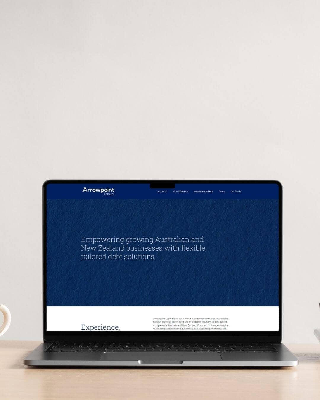 A laptop on a desk displays a website for Arrowpoint Capital, featuring text about tailored debt solutions for Australian and New Zealand businesses.