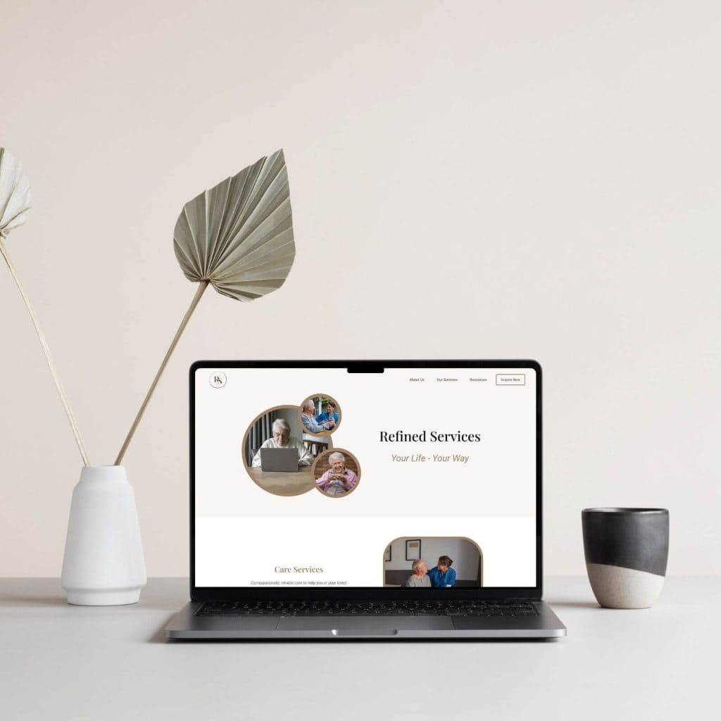 A laptop on a desk displays a webpage titled "Refined Services." Next to the laptop are a white vase with a dried leaf and a black-and-white cup.
